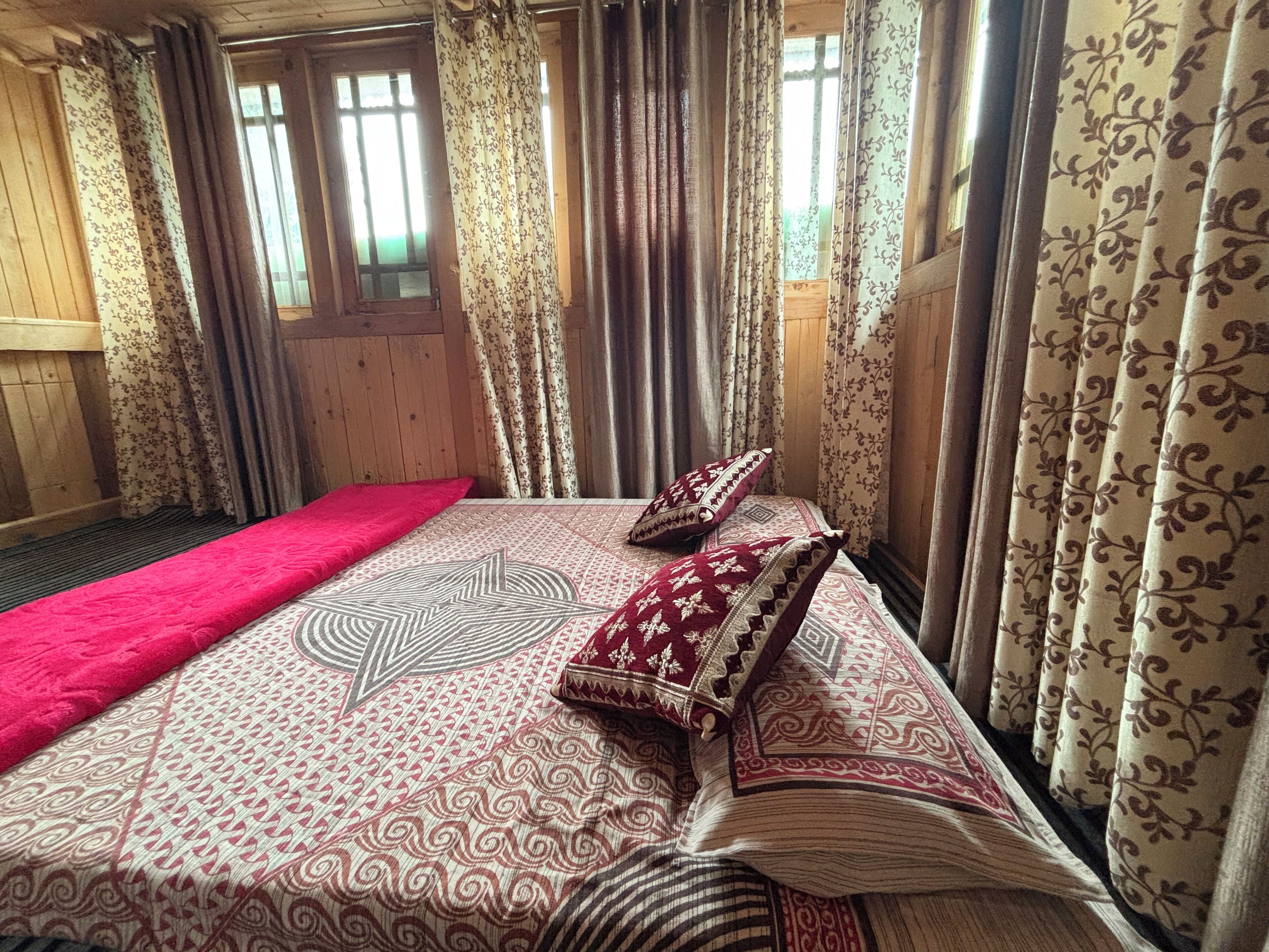 Una habitación con paredes de madera, una cama con ropa de cama estampada y cortinas con diseños florales.
