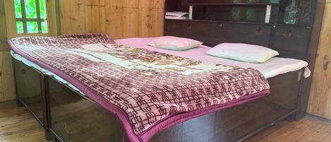 A bed with a patterned bedspread, a wooden headboard, and a window with green foliage outside.