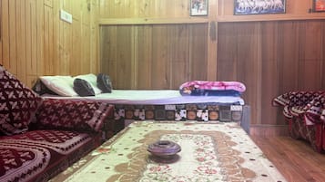 A room with wooden walls, a bed with a patterned bedspread, a sofa with a floral cover, and a decorative tablecloth.