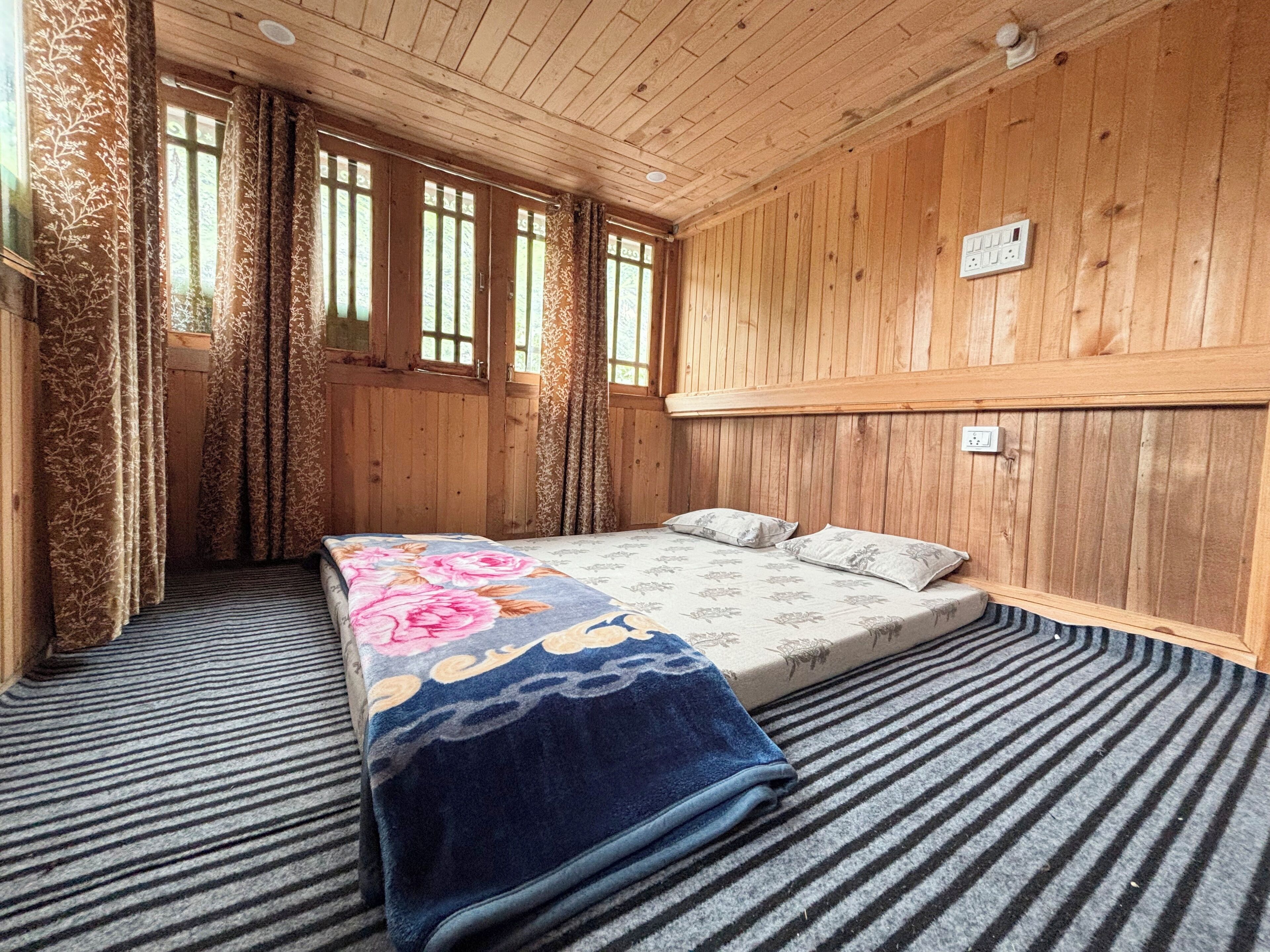 A wooden room with a bed, curtains, and a window.
