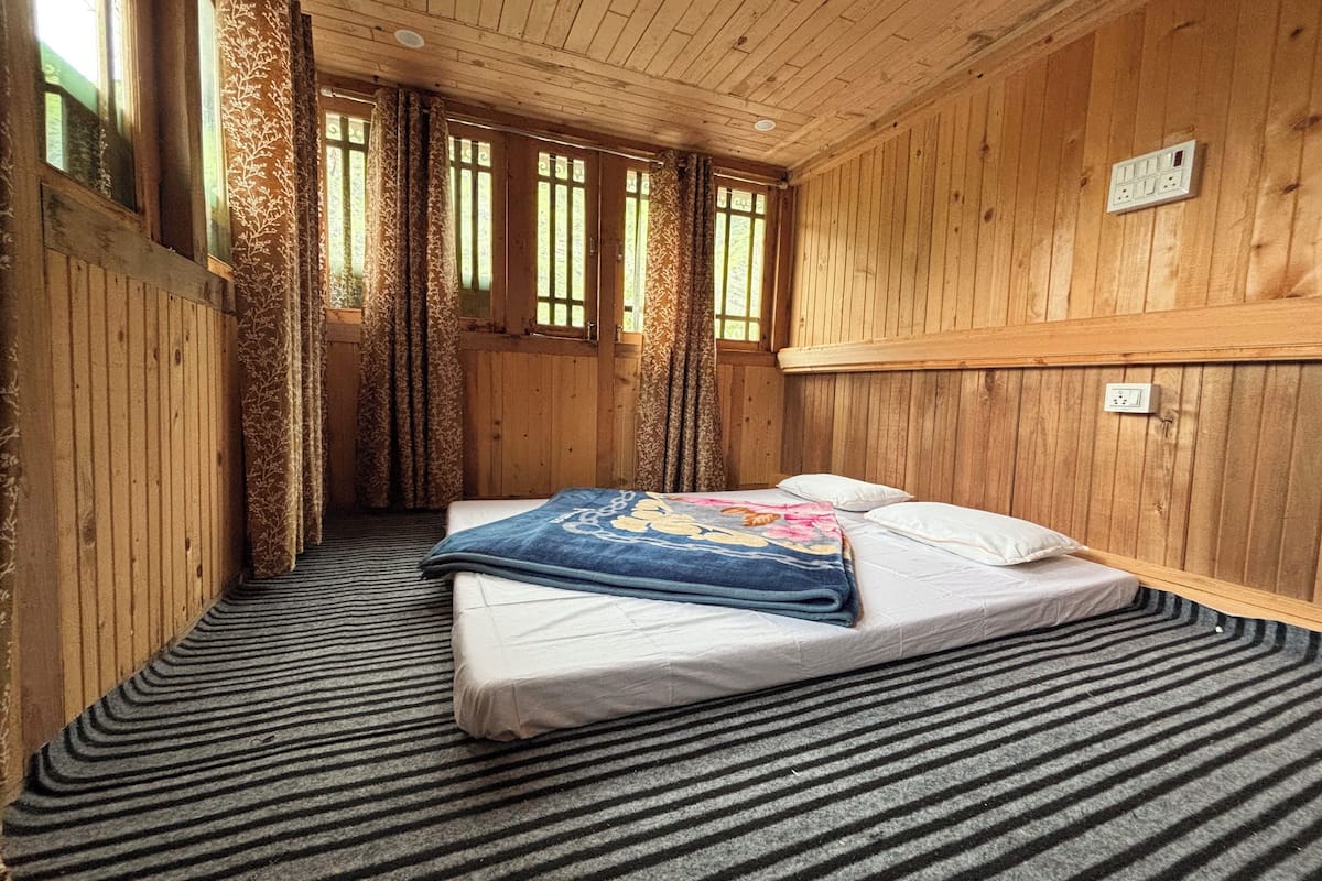 A wooden room with a bed, a window, and a power outlet on the wall.