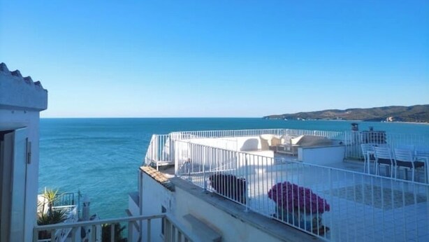 A balcony with a view of the sea, white railings, and a red umbrella.