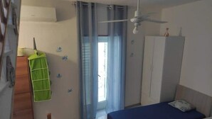 A bedroom with a bed, a wardrobe, a ceiling fan, and a window with curtains.