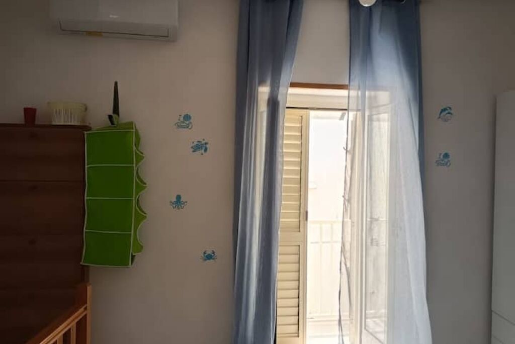 Una habitación con un aparador de madera, un estante verde y una ventana con cortinas azules.