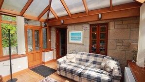 Una habitación acogedora con techo de madera, paredes de piedra, un sofá escocés y una puerta que da al exterior.