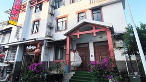 A multi-story building with a traditional architectural style, featuring a prominent entrance with a red and white facade, multiple windows, and a green artificial lawn in front.