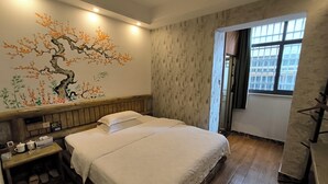 A neatly made bed in a hotel room with a wooden headboard, a wall mural, and a window with a view of the city.