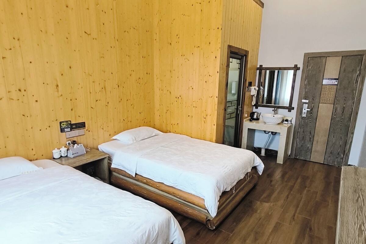 Et hotelværelse med to senge, trævægge, en trægulv, et badeværelse med vask og spejl, samt en dør med dekorativt panel.