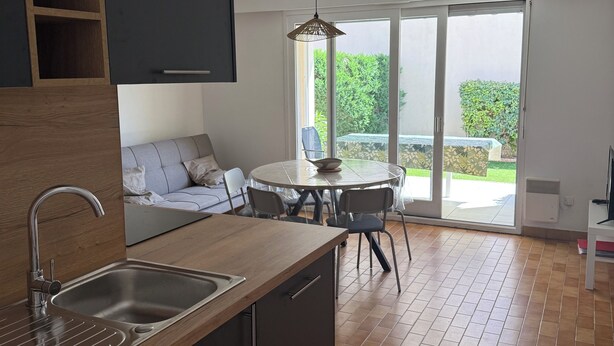 A modern kitchen with a wooden countertop, stainless steel sink, and a dishwasher. There is a dining area with a round table and chairs. - Cosy house 300m from the beach (La Tranche-sur-Mer)