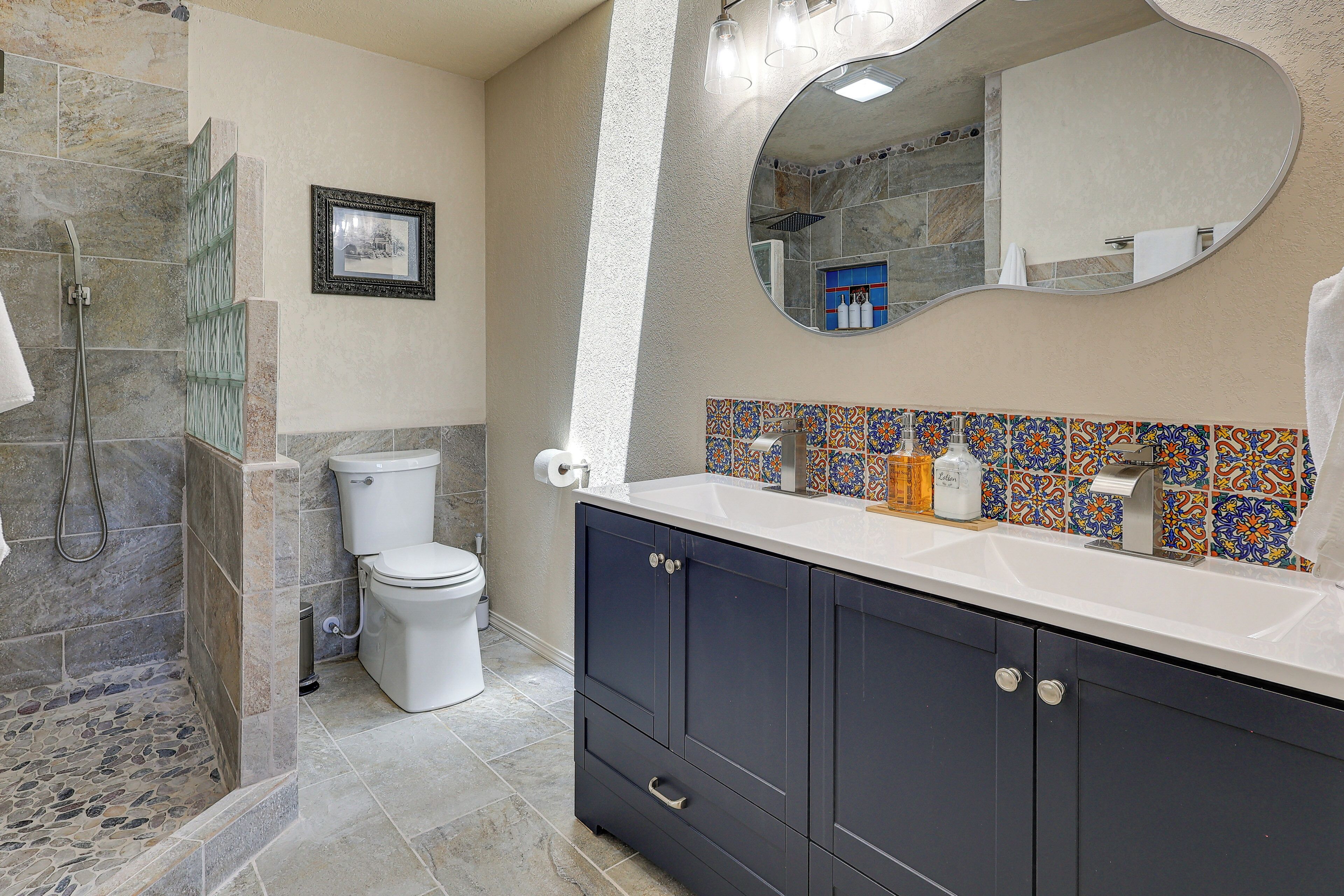 Un baño con ducha, inodoro, tocador con armarios, un espejo y salpicadero de azulejos.