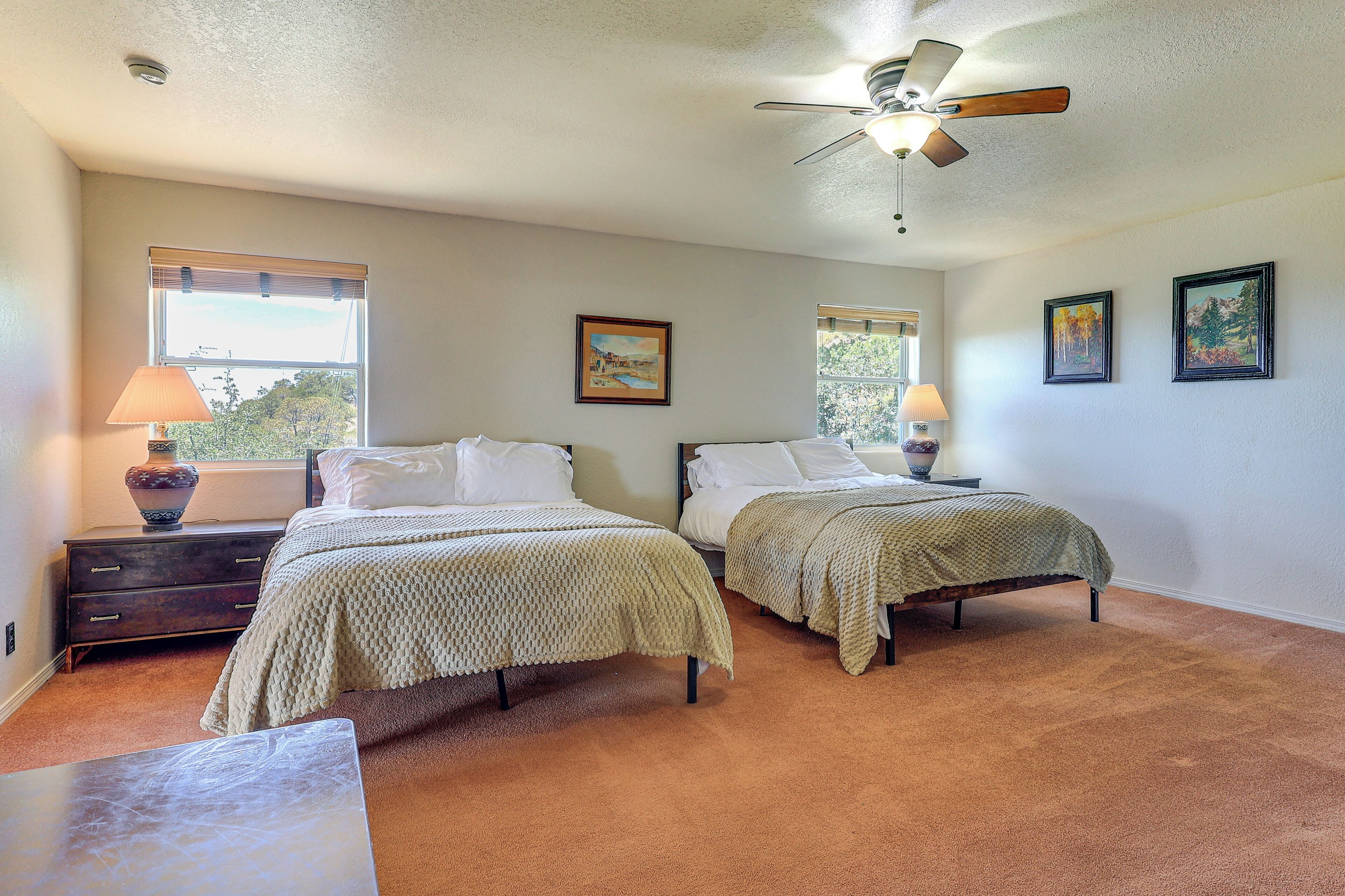 A bedroom with two beds, a ceiling fan, and artwork on the walls.