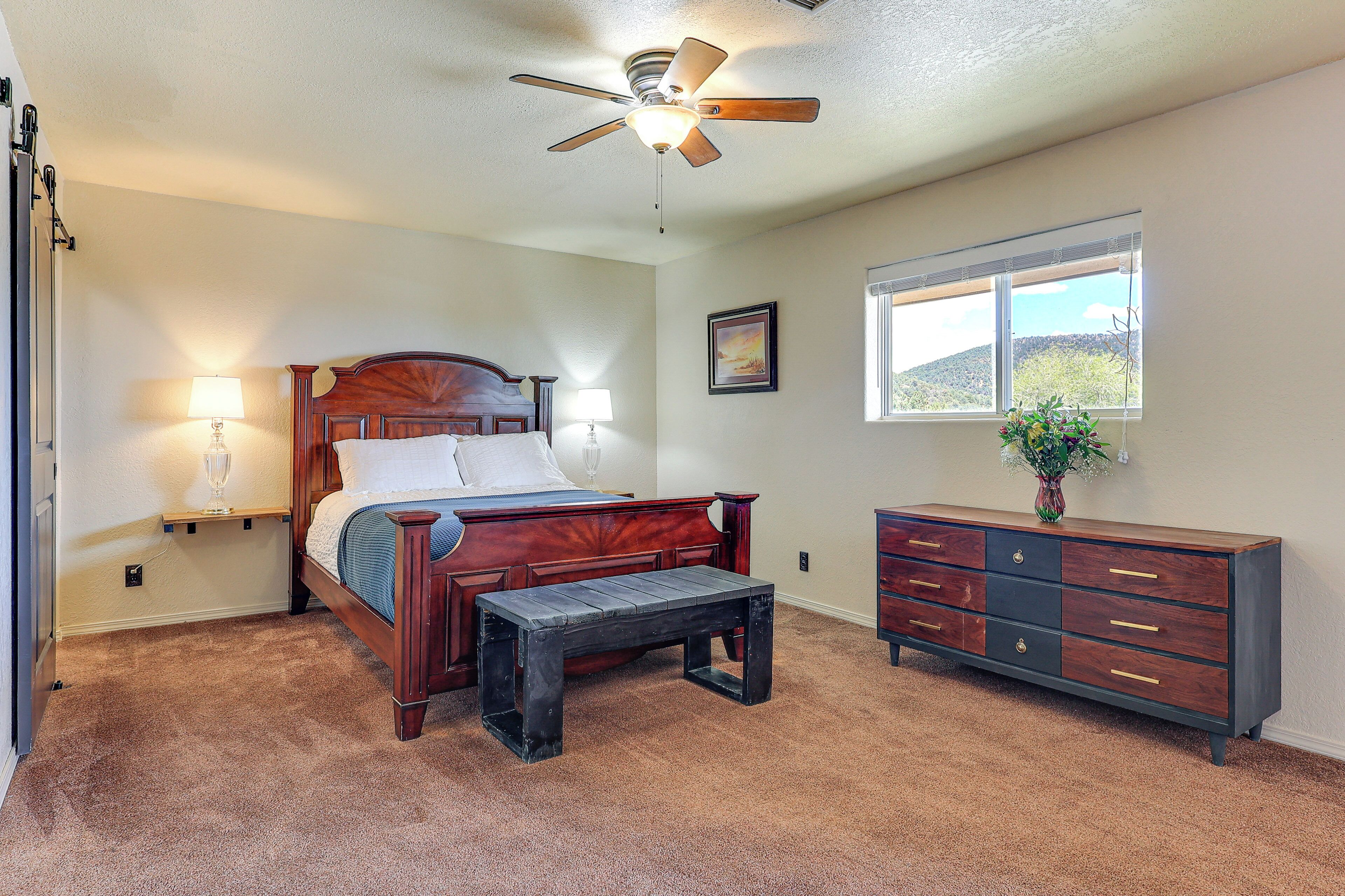 A bedroom with a wooden bed, bedside lamps, a wooden bench, a dresser, and a ceiling fan.