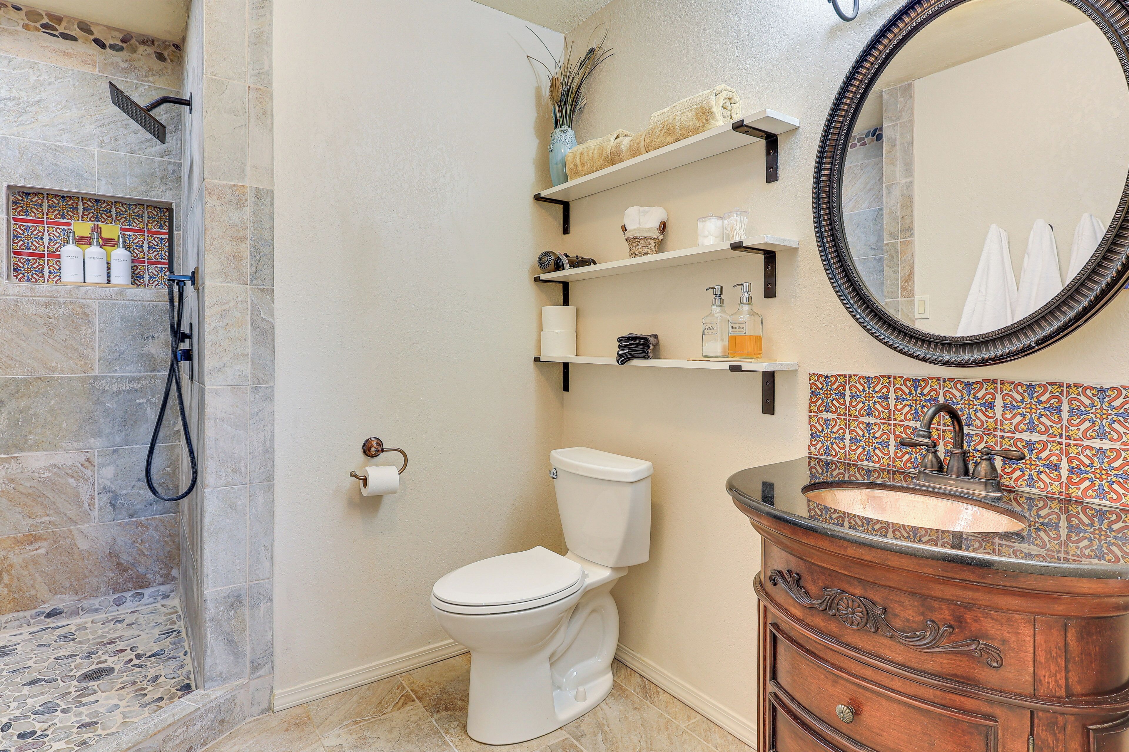 A bathroom with a shower, toilet, vanity, and shelves with toiletries.