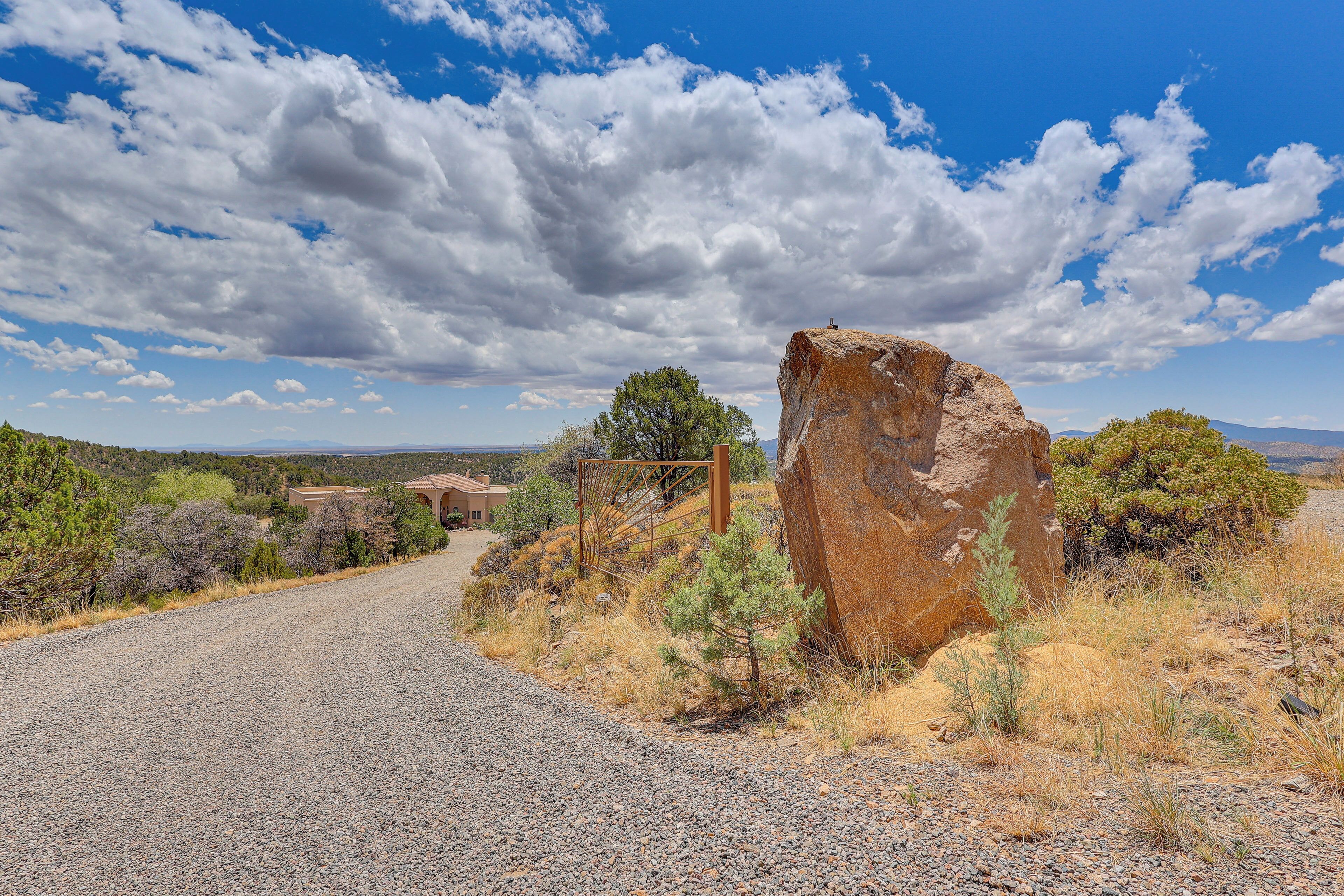 A gravel road leading to a rustic building with a large rock formation nearby.