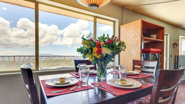 A dining table set with plates, glasses, and cutlery, a vase of flowers, and a view of the sky and mountains through large windows. - Panoramic Vistas and Spacious: Silver City Escape (Silver City)