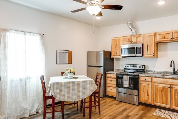 A kitchen with wooden cabinets, stainless steel appliances, a dining table with chairs, and a ceiling fan.
