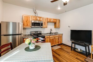 A modern kitchen with stainless steel appliances, wooden cabinets, a dining table with a placemat, and a flat-screen TV.