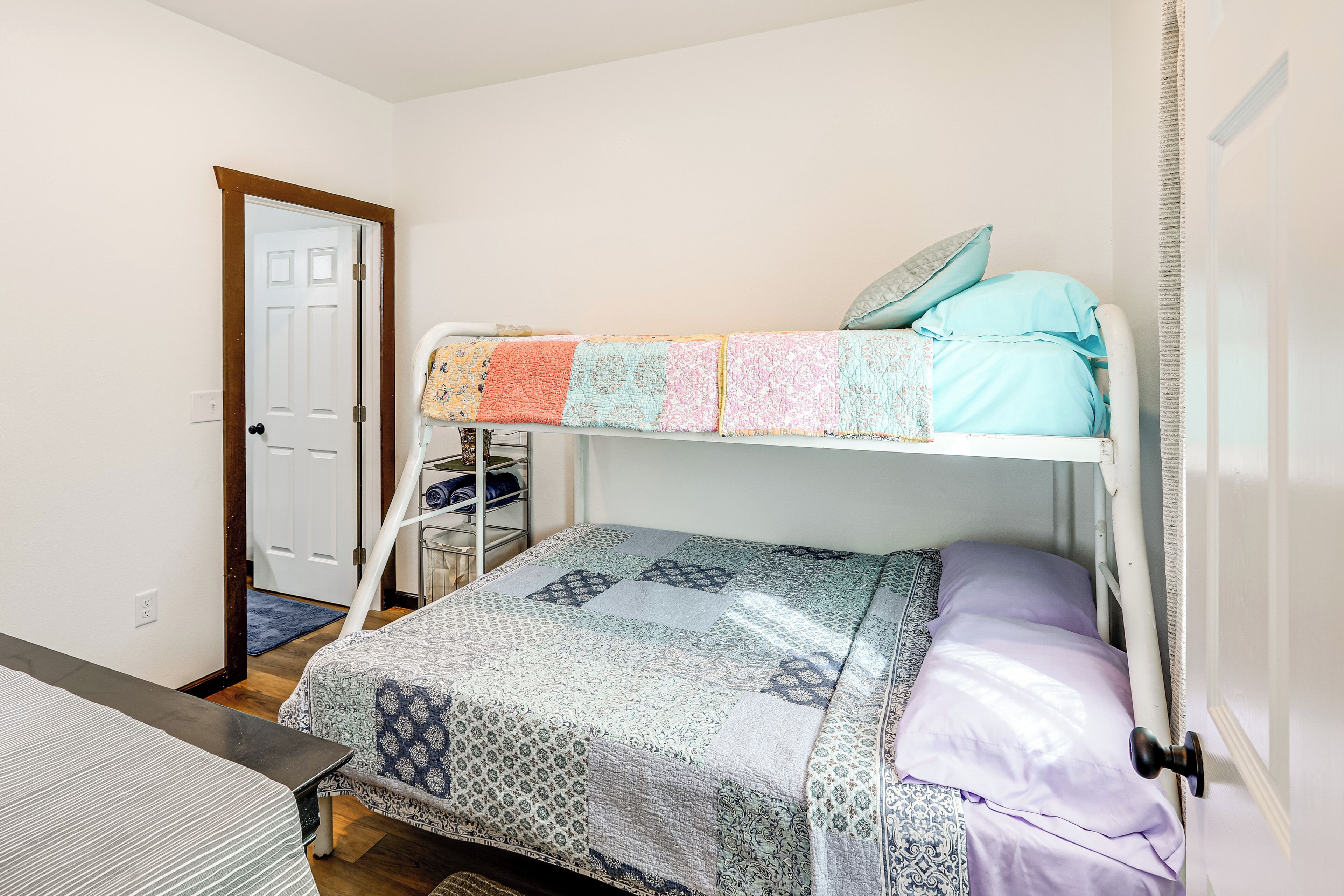 A bunk bed with a patterned bedspread and pillows, a small table, and a door in the background.