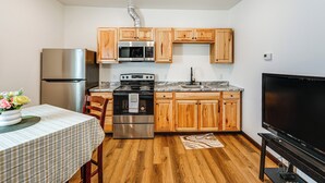 Una cocina compacta con armarios de madera, un refrigerador de acero inoxidable, un microondas, un horno y un televisor.