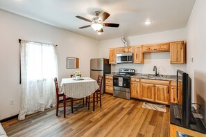 A compact kitchen with wooden cabinets, a stainless steel refrigerator, a microwave, an oven, and a ceiling fan.
