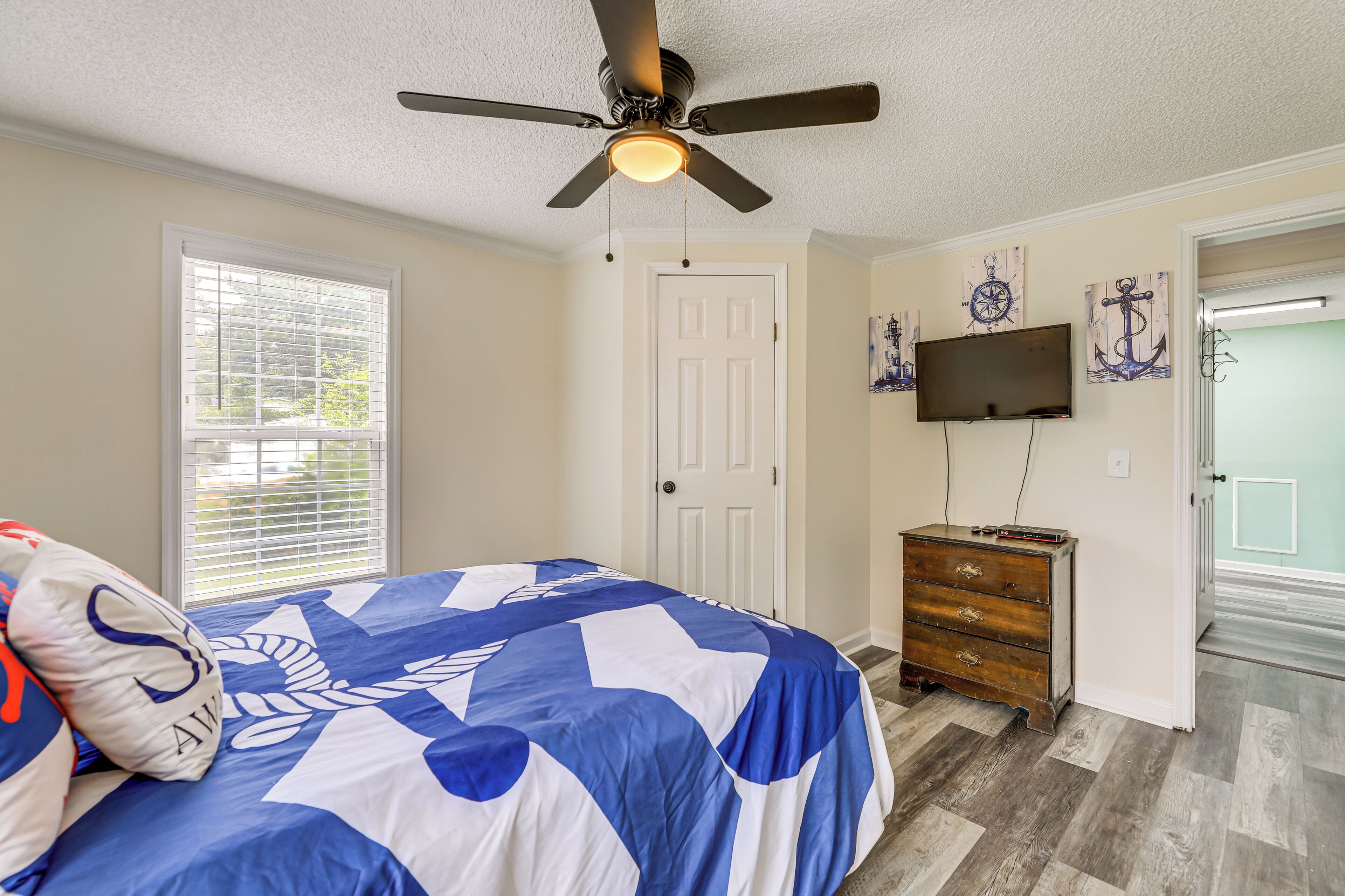 A bedroom with a bed, a ceiling fan, a dresser, a TV, and a door.