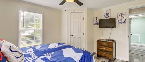 A bedroom with a bed, a ceiling fan, a dresser, a TV, and a door.