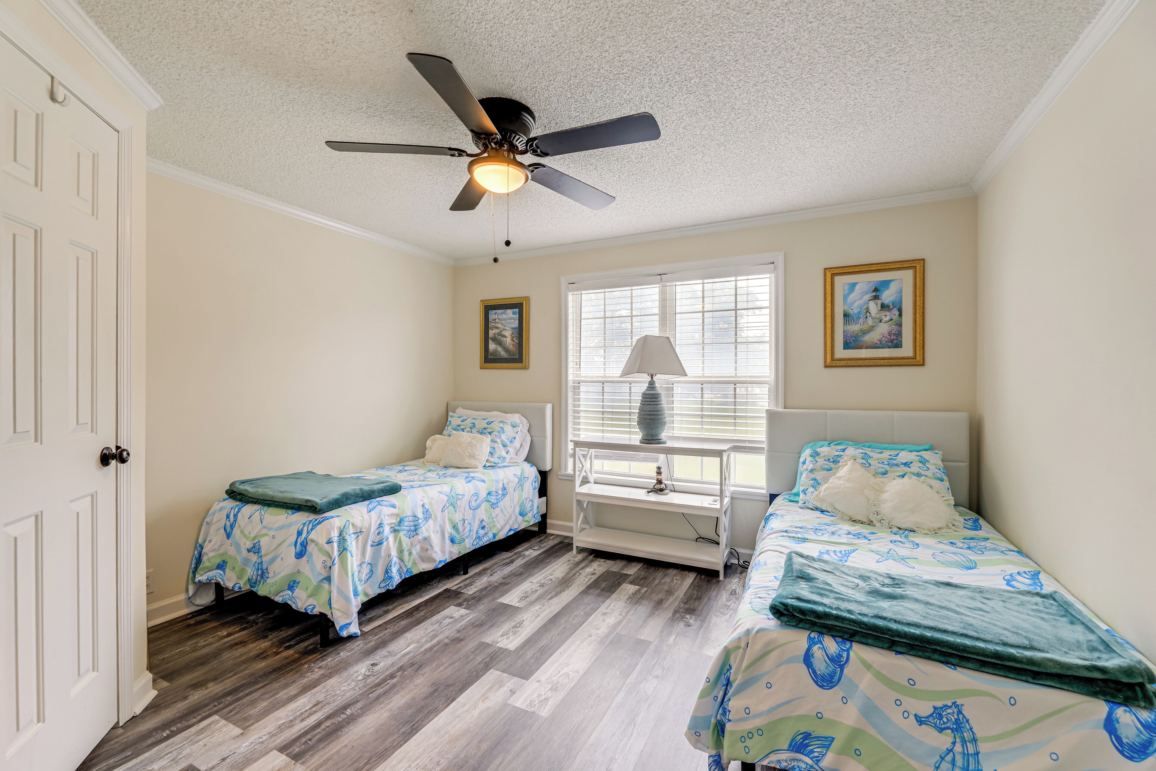 A bedroom with two beds, a ceiling fan, a window with blinds, and a door.