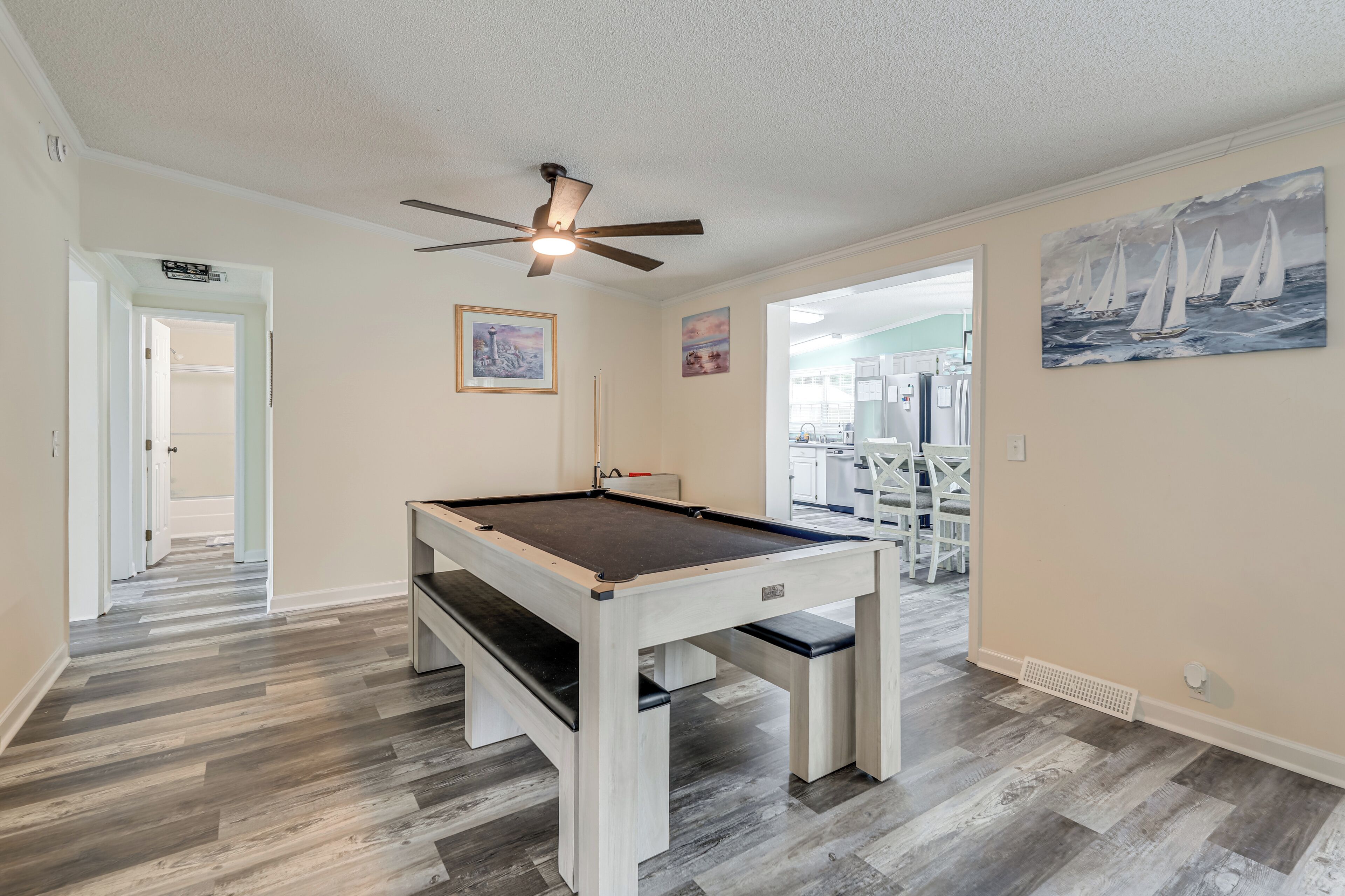 A pool table in a room with hardwood floors, a ceiling fan, and artwork on the walls.