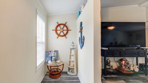 Un couloir doté d’un plancher en bois, d’un gouvernail de bateau fixé au mur, d’une étagère ornée d’objets décoratifs sur le thème de la marine, et d’un bureau avec un ordinateur et divers objets décoratifs.