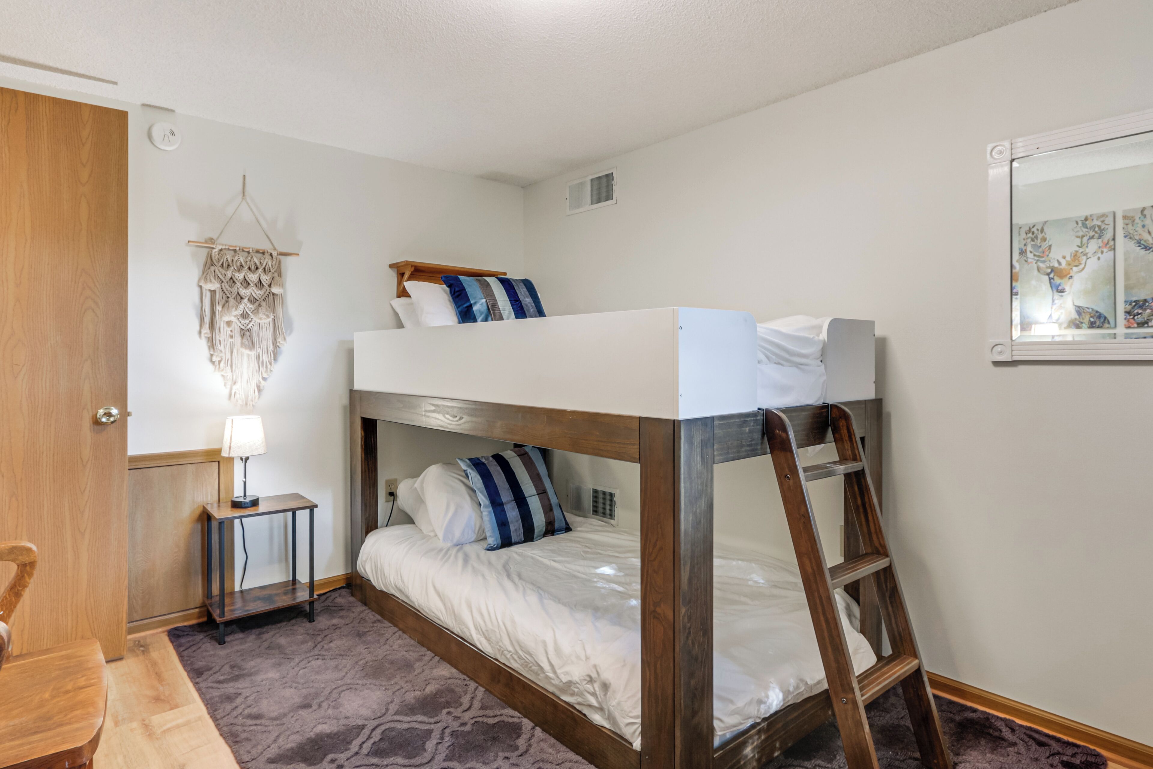 Une chambre avec un lit superposé, une échelle, une petite table avec une lampe et une décoration murale.
