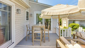 En træterrasse med et bord, stole og en stor parasol, samt et hvidt hegn.