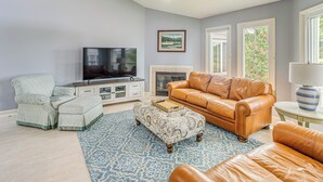 A living room with a television, a fireplace, and a leather sofa. - Marina & Pool: Roomy Golf-view Home in Southport (St. James)