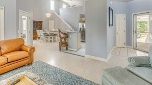 A spacious living area with a leather sofa, a patterned rug, and a dining area with a kitchen in the background. - Marina & Pool: Roomy Golf-view Home in Southport (St. James)