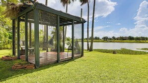 Een overdekt terras met uitzicht op een meer en palmbomen.