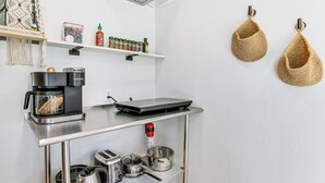 Een kitchenette met een koffiezetapparaat, toaster, waterkoker en pannen op een roestvrijstalen aanrecht.