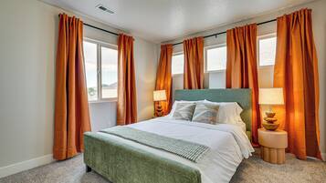 Un dormitorio ordenado con cama, dos mesitas de noche y una ventana con cortinas.