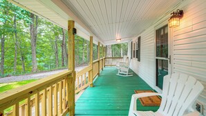 A covered porch with a green floor, wooden railing, and a white rocking chair. - Secluded Lodge Stay: Day Trip to Audra State Park! (French Creek)