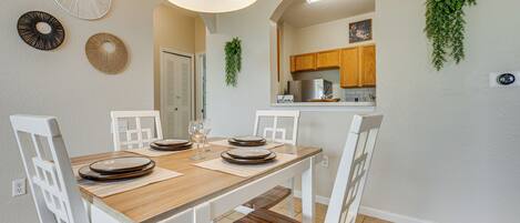 Comedor con mesa de madera dispuesta para cuatro, sillas blancas y lámpara colgante.