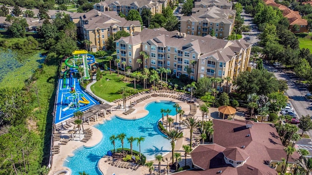 An aerial view of a resort with a large swimming pool, a water park, and multiple buildings with balconies.
