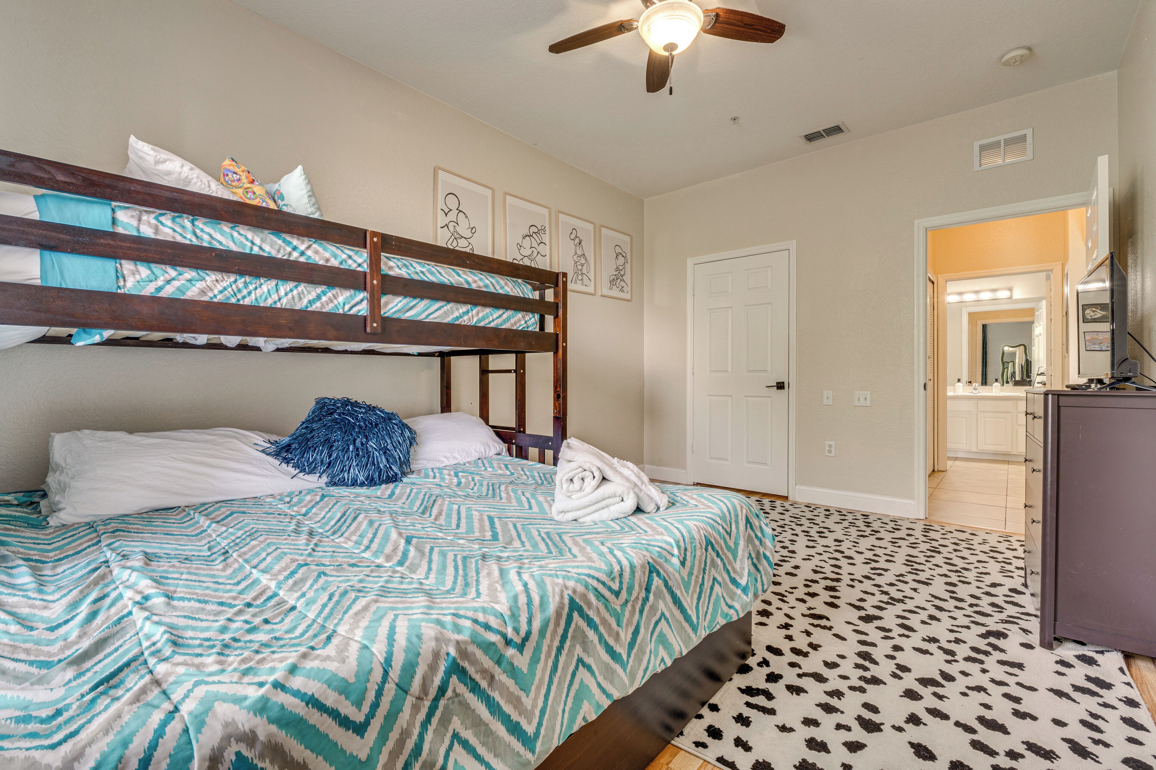 A bedroom with a bunk bed, a patterned bedspread, a ceiling fan, and a patterned rug.