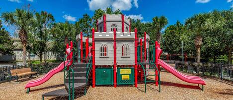 A playground with two red slides, a climbing structure, and a bench.