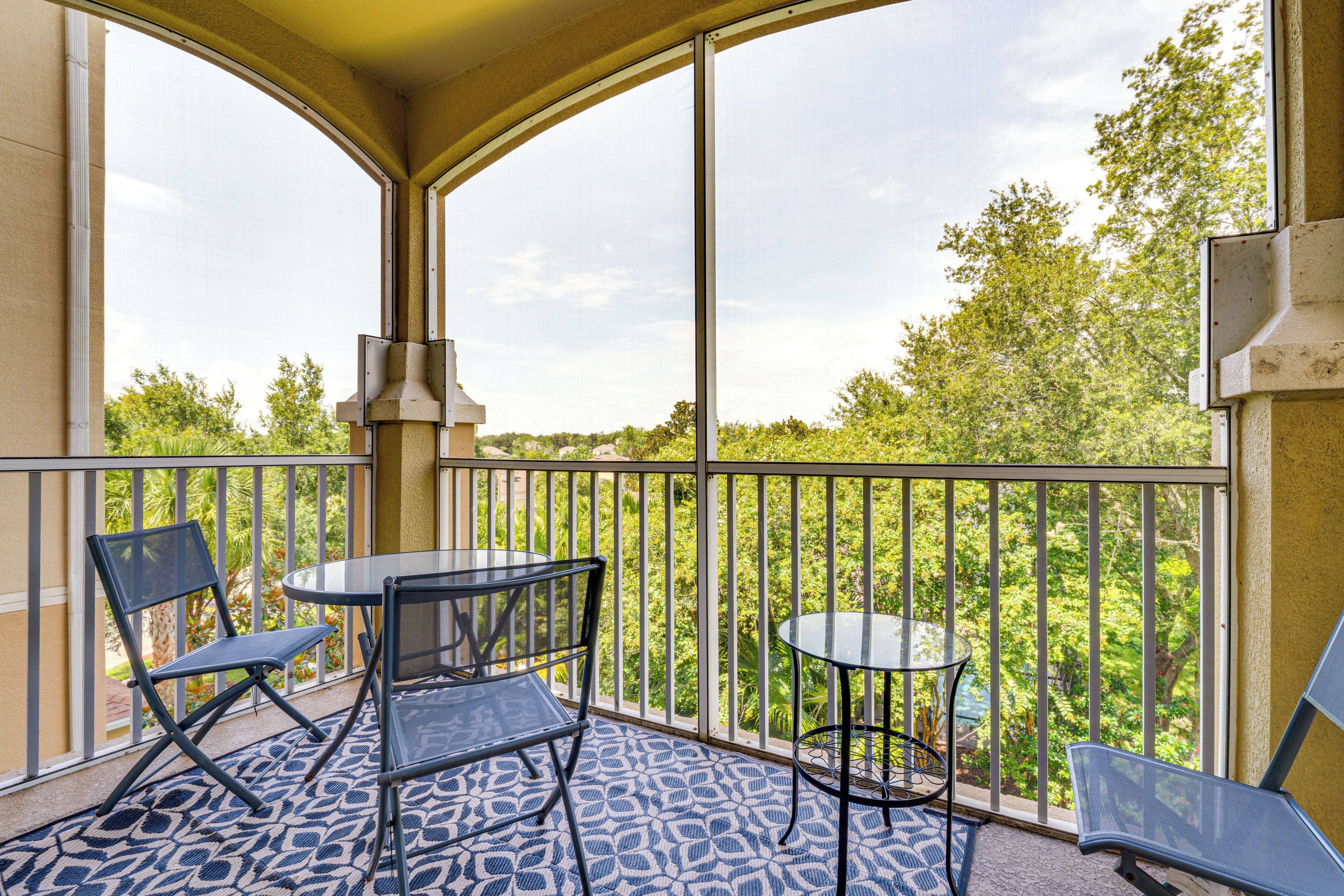 A balcony with two tables and chairs, a patterned floor, and a view of greenery.