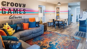 A modern living room with a gray sofa, colorful pillows, a vibrant rug, and a wall sign reading 'Groovy Games Getaway.' - 'groovy Games Getaway' Holiday Stay in Branson! (Branson)
