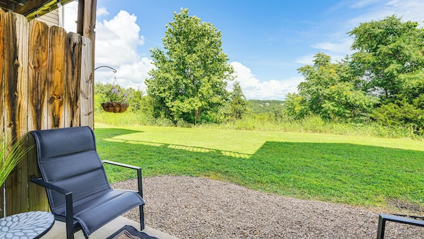 A patio with a black chair and table, a wooden fence, and a view of a grassy area with trees. - 'groovy Games Getaway' Holiday Stay in Branson! (Branson)