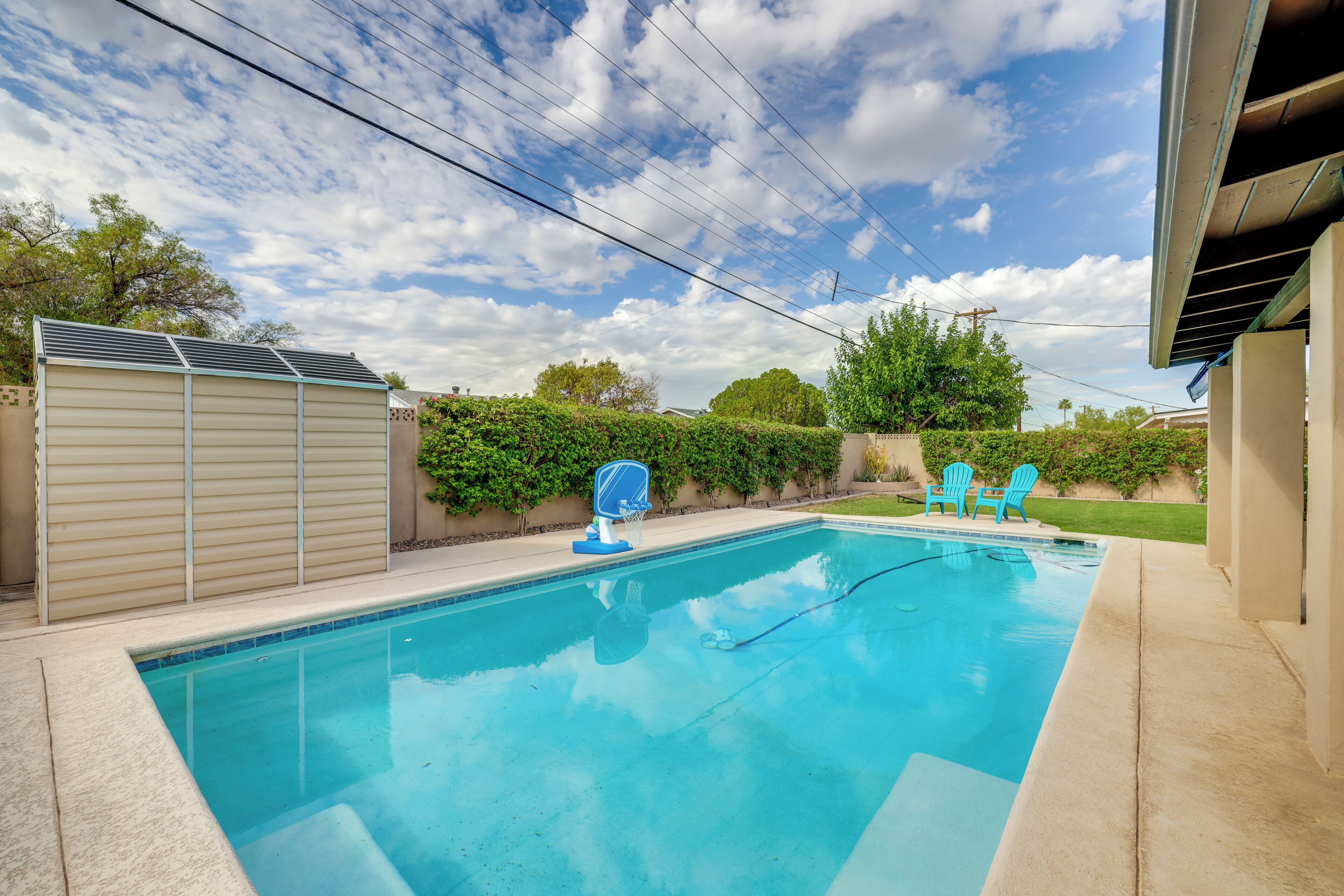 A rectangular swimming pool with a built-in basketball hoop, surrounded by a concrete deck.