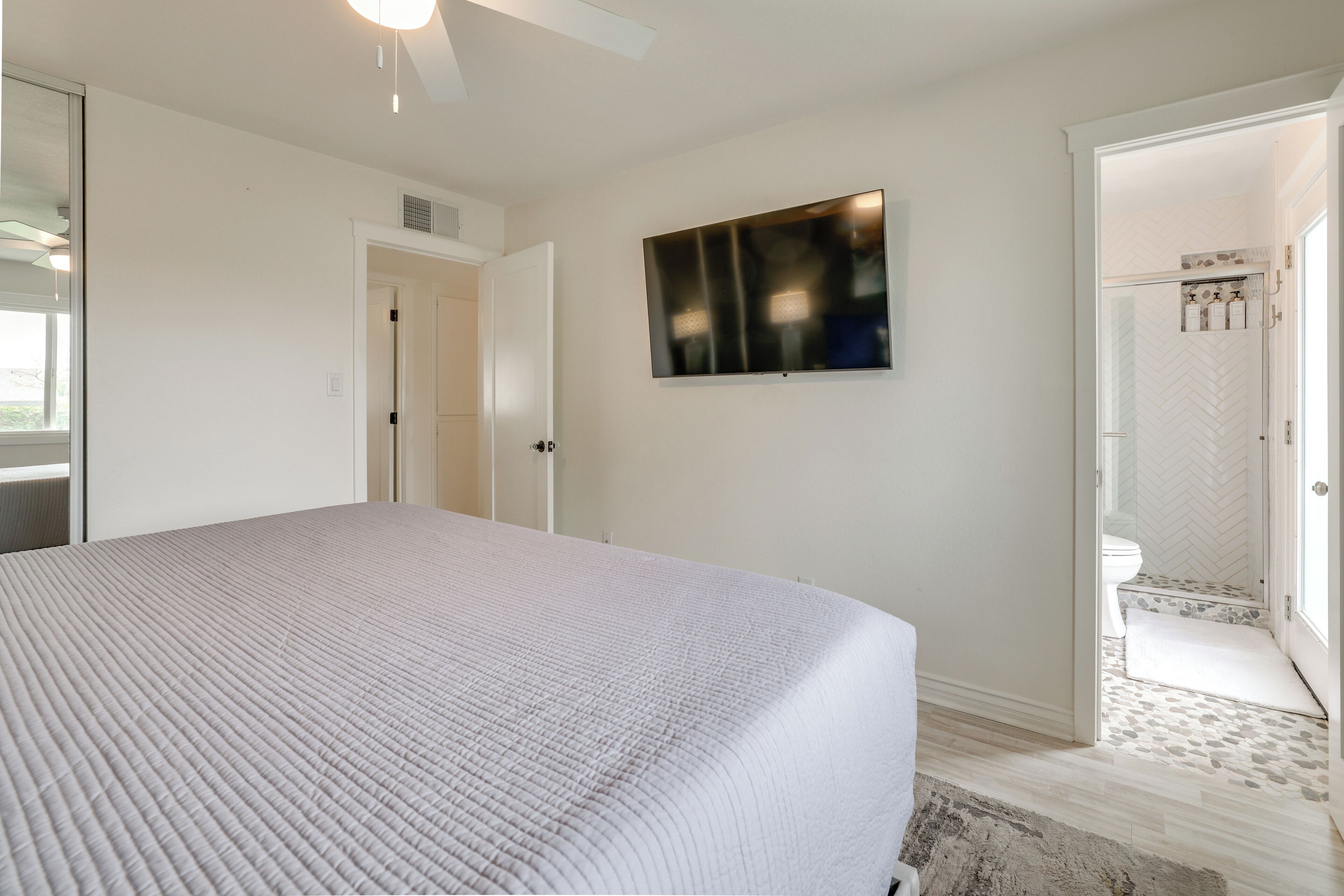 Een slaapkamer met een groot bed, een flatscreen televisie aan de muur en een deur naar een badkamer.
