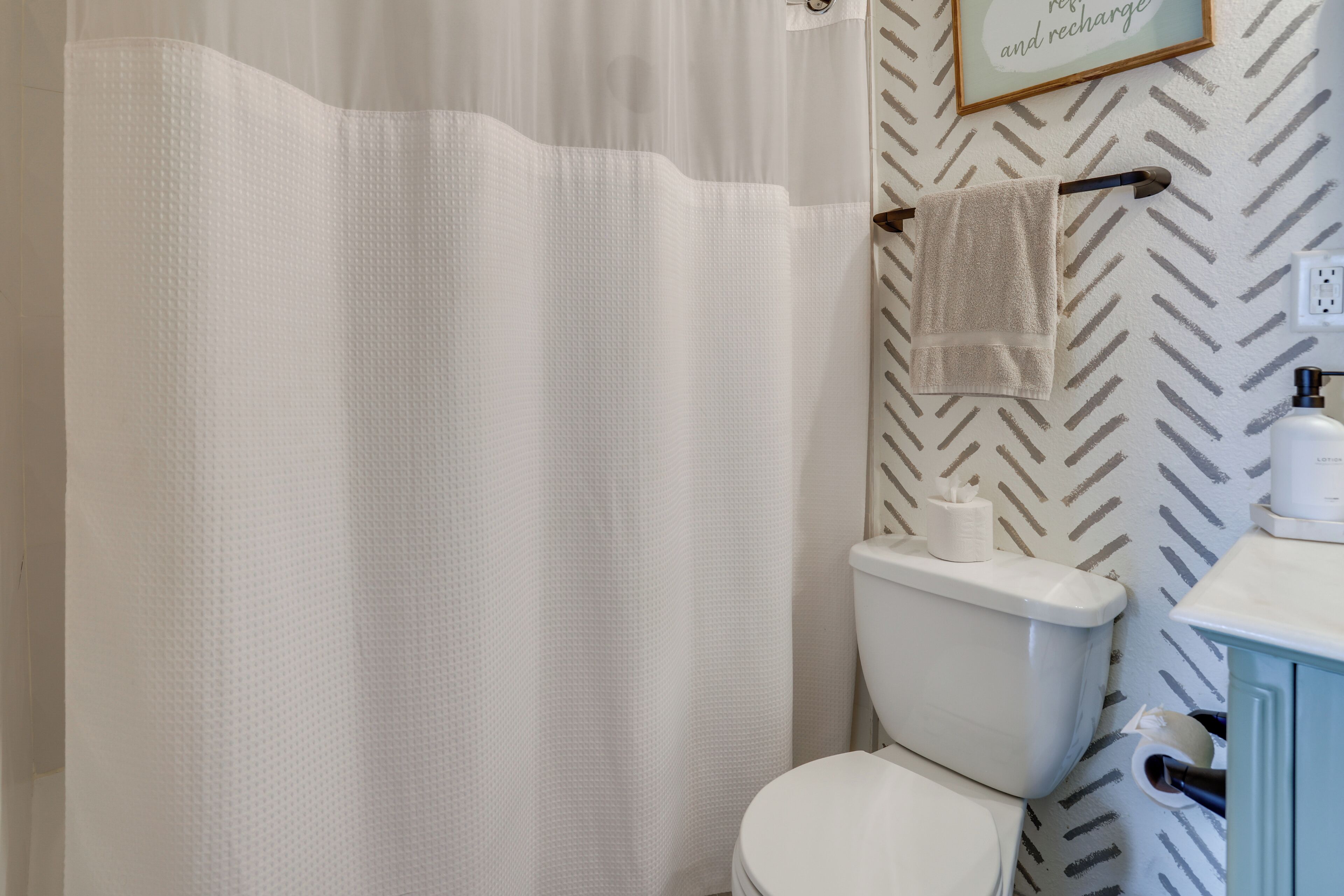 A bathroom with a white shower curtain, a toilet, and a sink with a towel hanging on the wall.