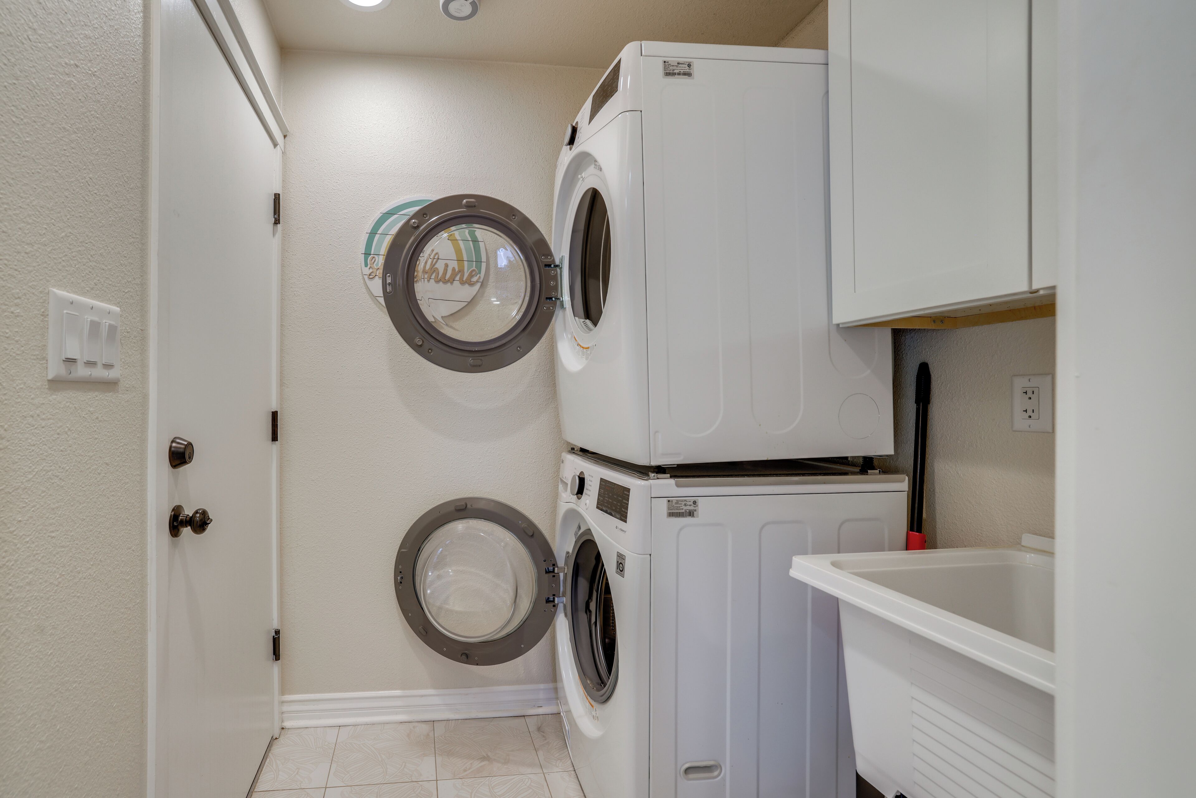 A laundry room with two stacked front-loading washing machines and a white sink.