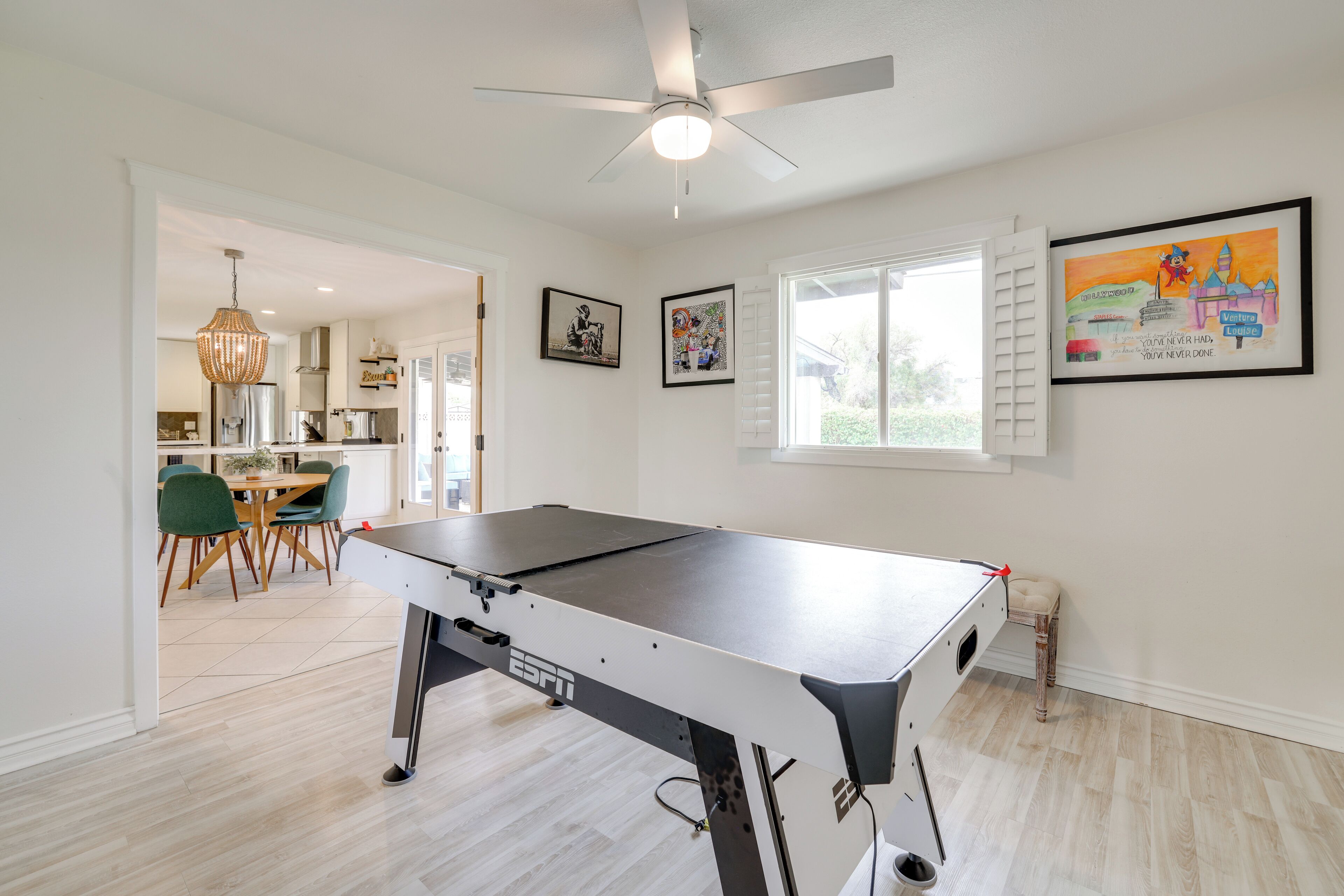 A room with a pool table, a ceiling fan, and a window with a view of greenery.