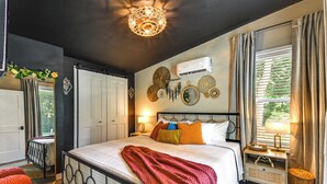 A bedroom with a bed, bedside tables, a wall-mounted air conditioner, decorative wall art, and a window with curtains. - Hike & Fish: Nature Escape Near Licking River! (Cynthiana)